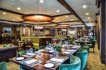 The image shows an elegantly set restaurant with green seating, wooden tables, and ambient lighting.