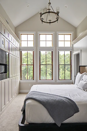A spacious bedroom with tall windows, a large bed, a cozy gray blanket, and elegant white walls.