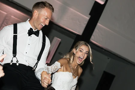 A couple is joyfully celebrating, possibly at a wedding, dressed in formal attire and laughing, while being lifted up.