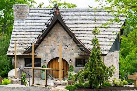 A quaint stone cottage with a steep roof, circular wooden door, and greenery around it, creating a fairy-tale appearance.