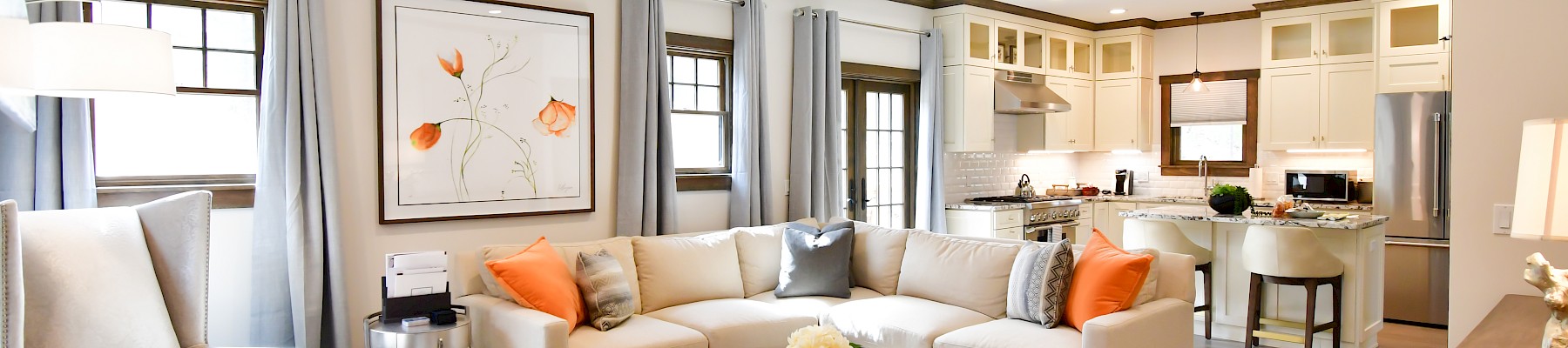 The image shows a modern living room and kitchen with a beige sectional sofa, armchairs, and a wooden coffee table on a rug.